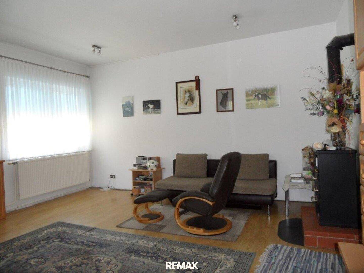 Gemütliches Wohnzimmer mit Sofa, Sessel, Holzofen und hellem Parkettboden.