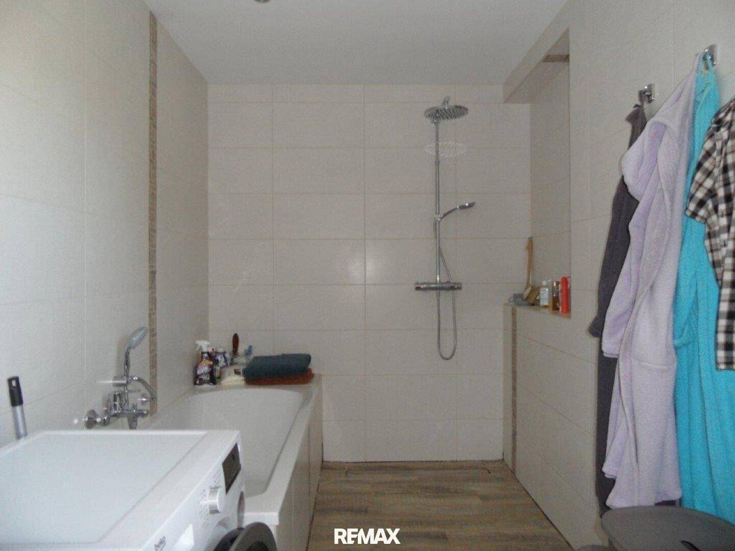 Modernes Badezimmer mit Badewanne, Duschbereich und Waschmaschine, hell gefliest.
