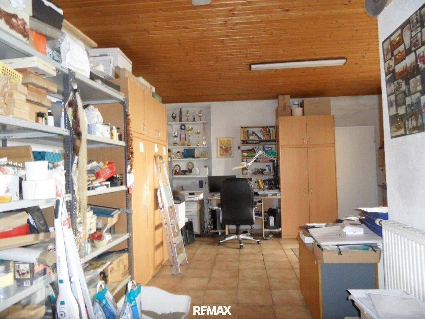 Geräumiges Büro mit Holzdecke, Regalen und einem Arbeitsbereich, auch als Lagerraum nutzbar.