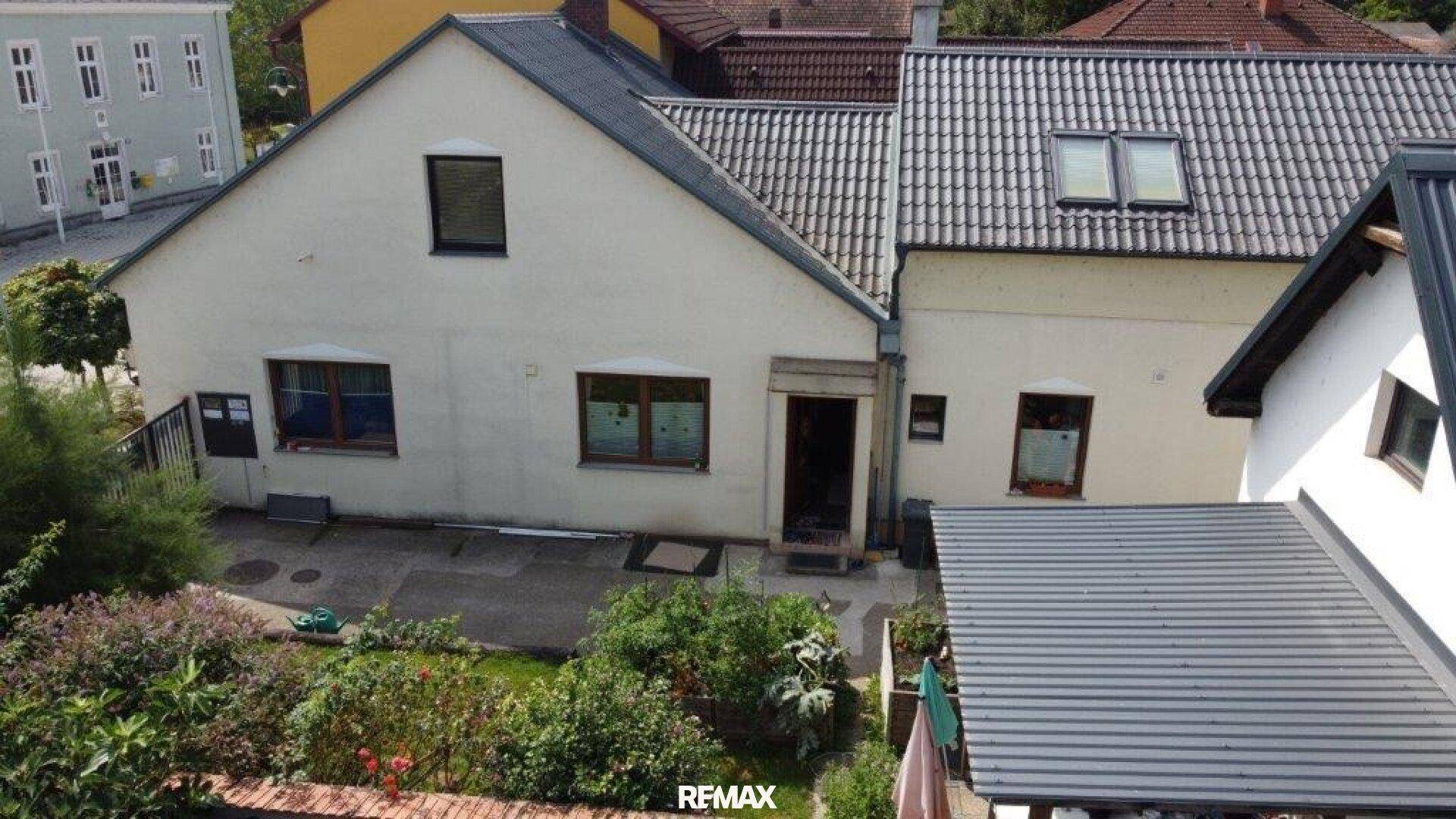 Rückansicht eines Hauses mit einem gepflegten Garten und einer kleinen gepflasterten Terrasse.