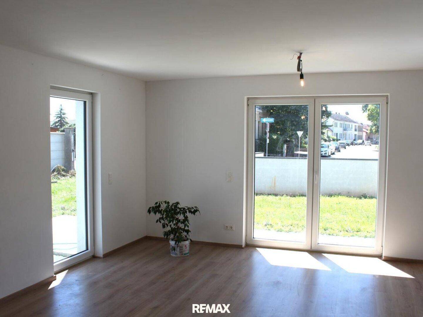 Heller Wohnraum mit großen Fenstern und Zugang zum Garten, ausgestattet mit Holzboden.