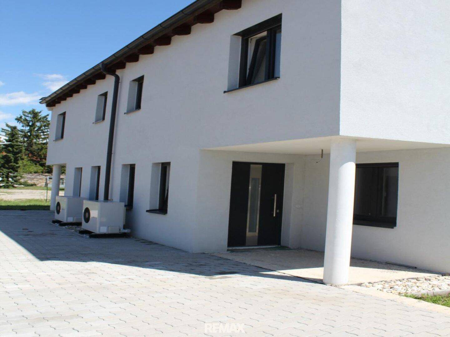 Eingangsbereich des modernen Hauses mit Vordach und Säulen sowie Wärmepumpen an der Seite.