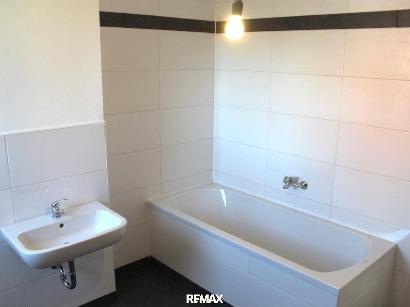 Funktionales Badezimmer mit weiß gefliesten Wänden, einer Badewanne und einem Waschbecken.