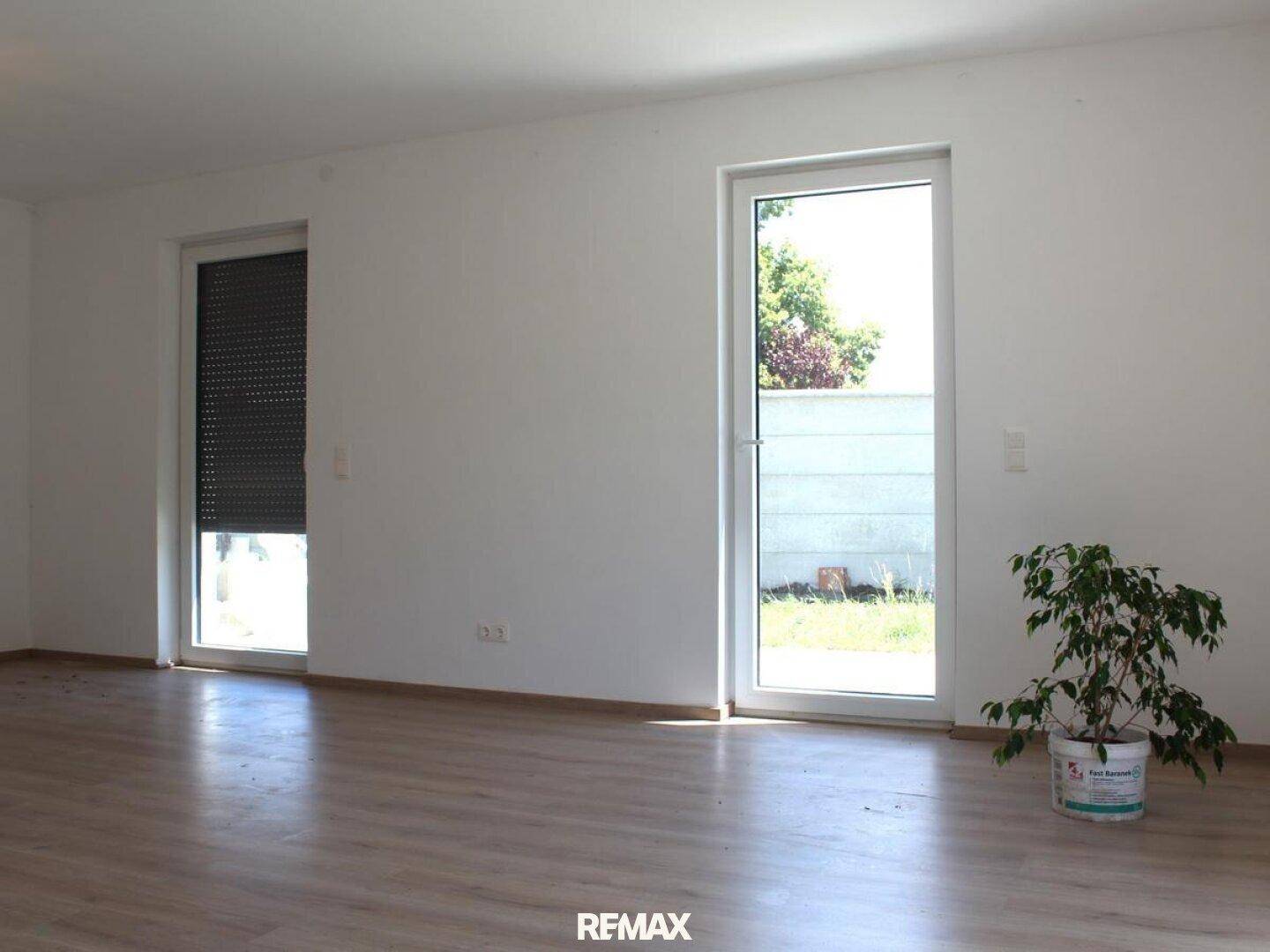 Heller Wohnraum mit Laminatboden, großen Fenstern und einem heruntergelassenen Rollladen.