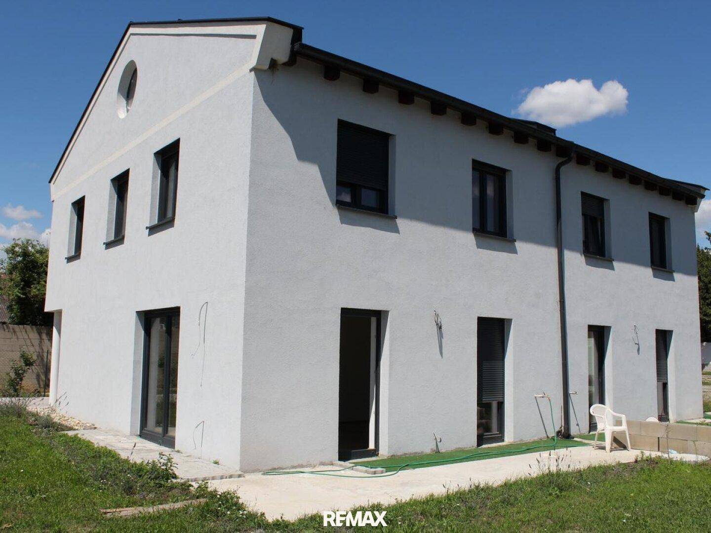 Neubau-Doppelhaushälfte mit heller Fassade und modernen dunklen Fenstern in sonniger Lage.