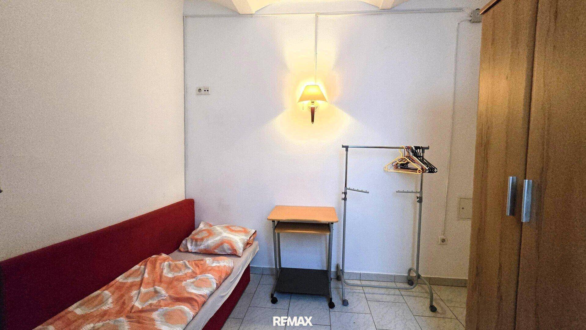 Kleines Schlafzimmer mit Einzelbett, einem Beistelltisch und einem Kleiderständer.