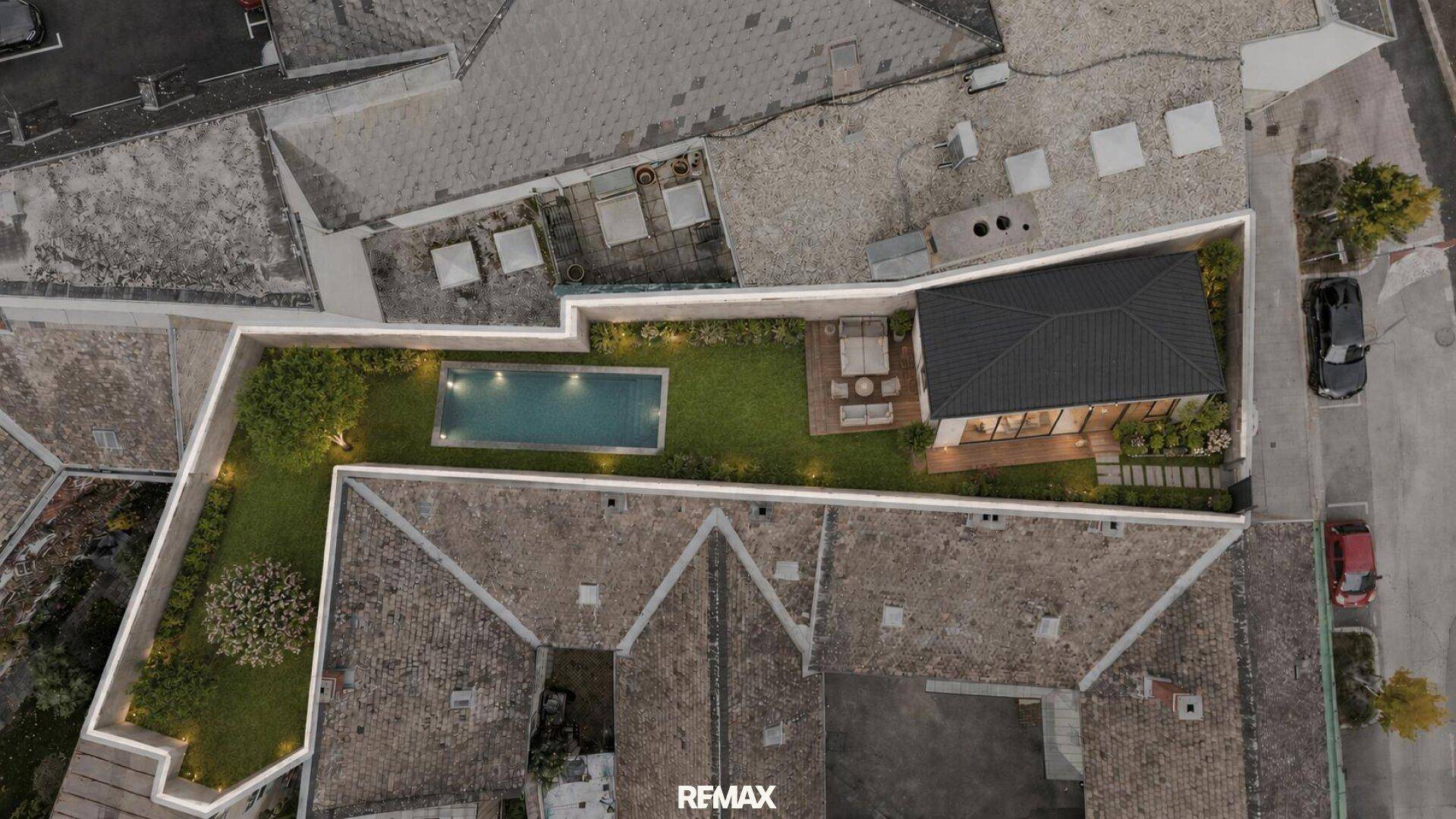Luftaufnahme eines Anwesens mit Pool, Garten und möblierter Terrasse, umgeben von historischen Dächern.
