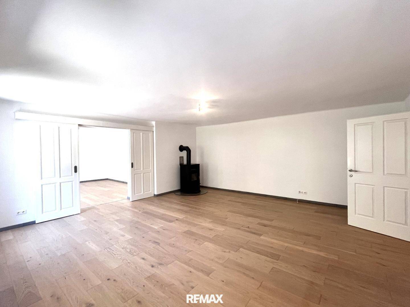 Großes Wohnzimmer mit Holzboden und einem modernen Holzofen als Wärmequelle.