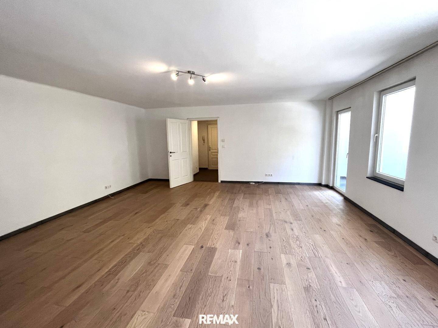 Heller Wohnbereich mit Holzboden und Zugang zu einem weiteren Raum, ideal für flexible Nutzung.