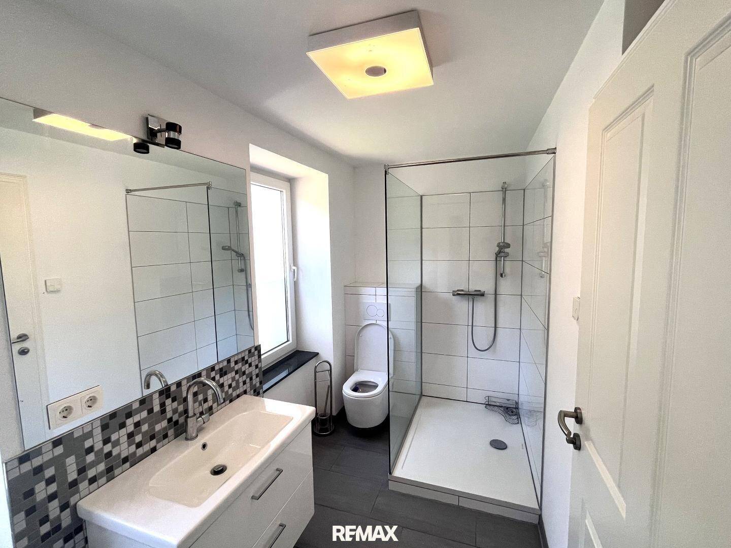 Modernes Badezimmer mit ebenerdiger Dusche, Waschbecken und Fenster für Tageslicht.
