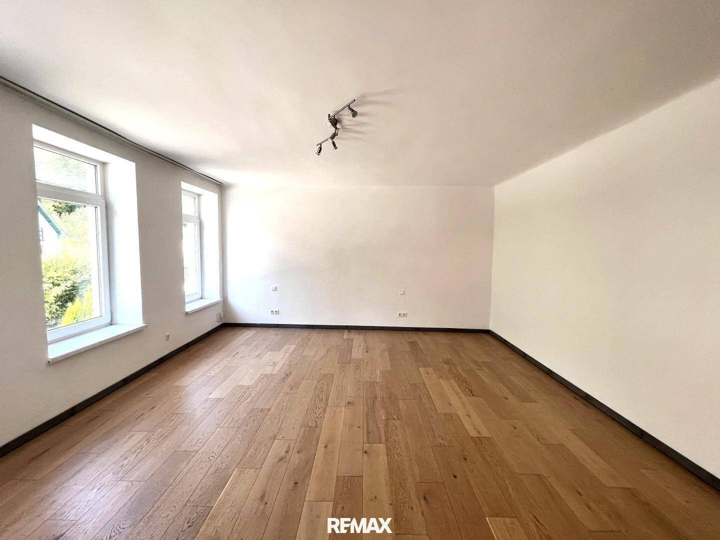 Helles und geräumiges Zimmer mit Holzboden und großen Fenstern.
