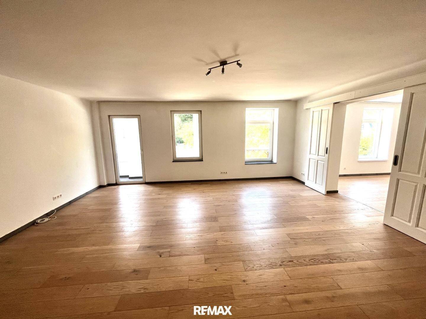 Geräumiges Wohnzimmer mit hellem Holzparkett und Zugang zu weiteren Räumen.