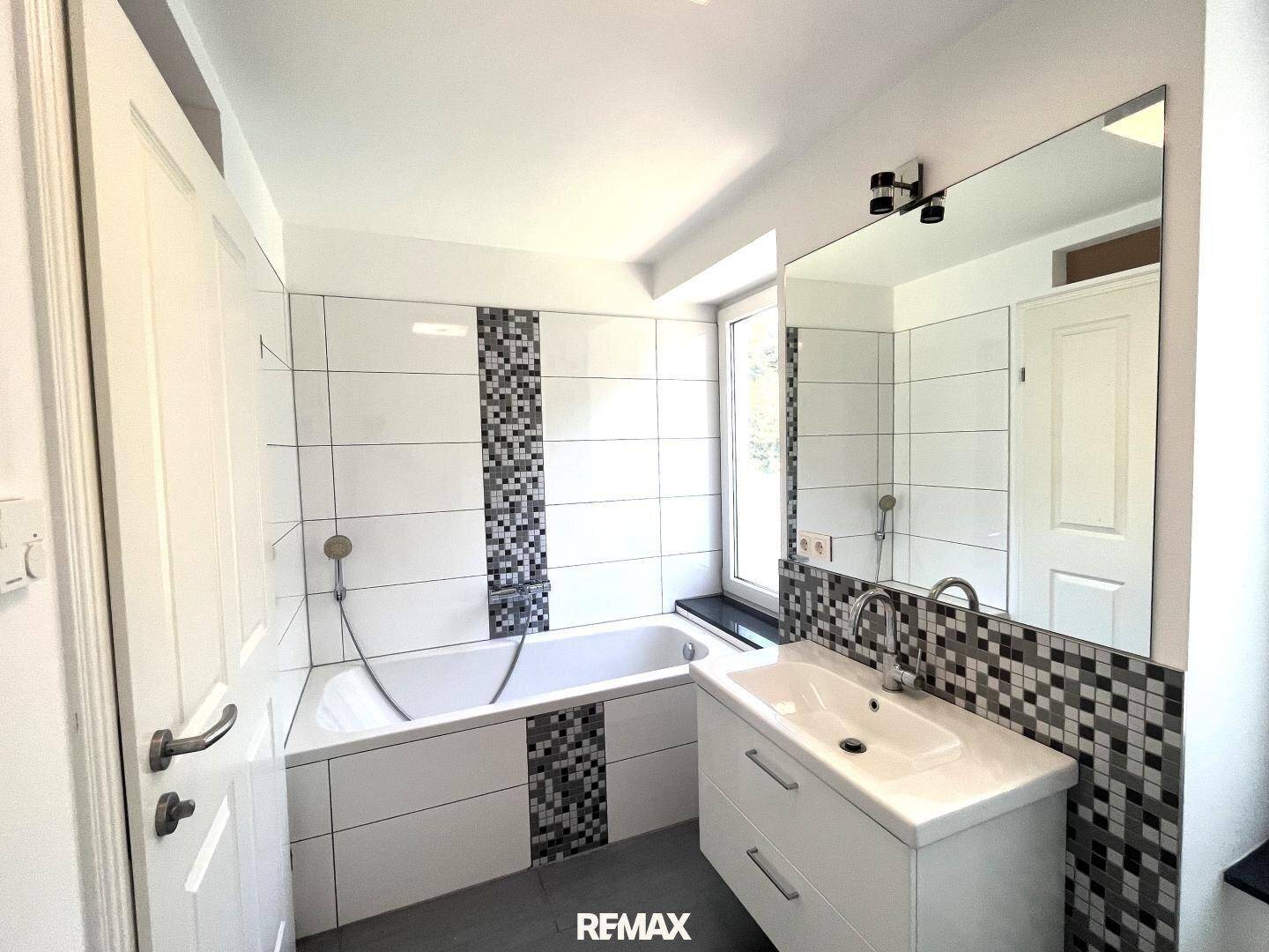 Helles Badezimmer mit Badewanne, Waschbecken und modernem Fliesendesign.