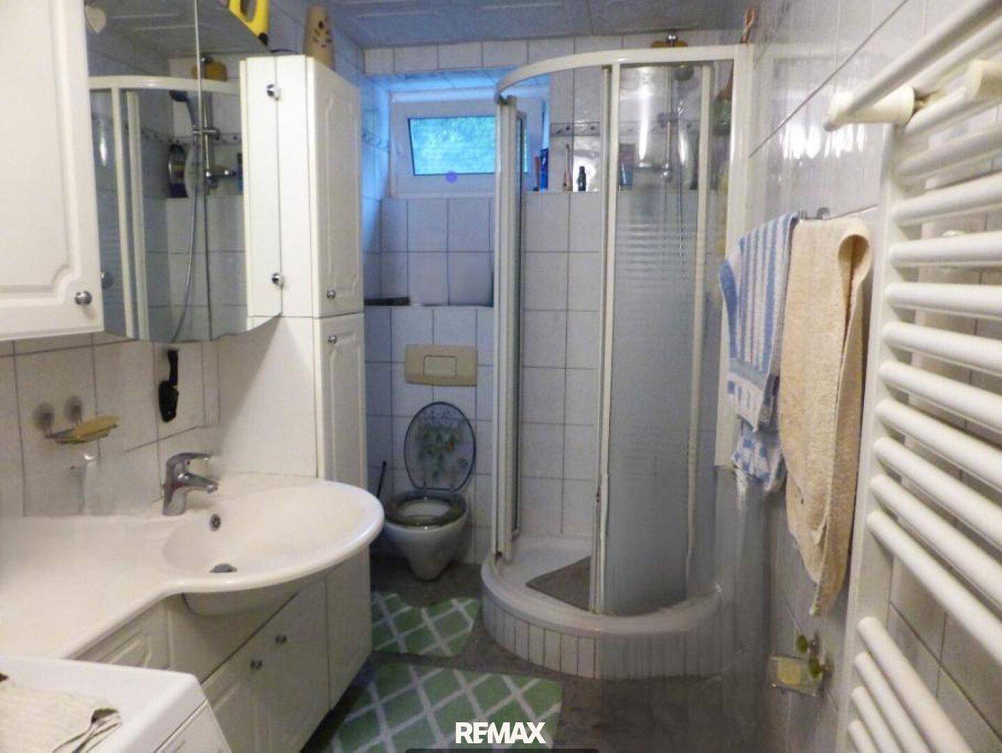 Badezimmer mit Duschkabine, Waschbecken, Toilette und beheiztem Handtuchhalter.