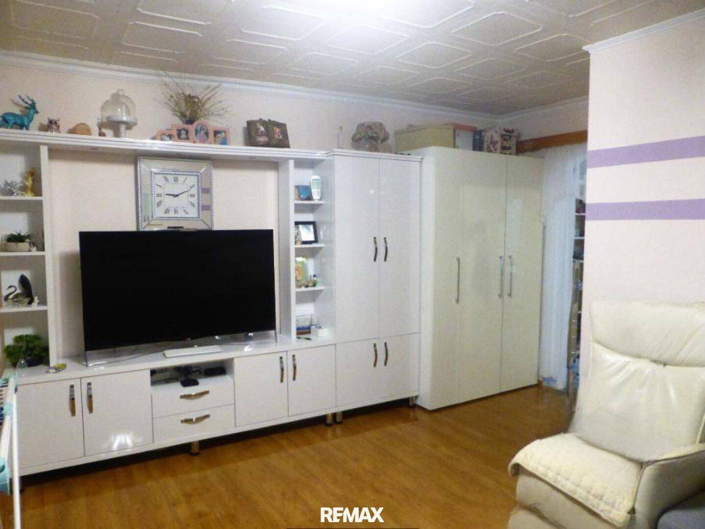 Gemütliches Wohnzimmer mit großem TV-Möbel, weißen Schränken und einer strukturierten Decke.