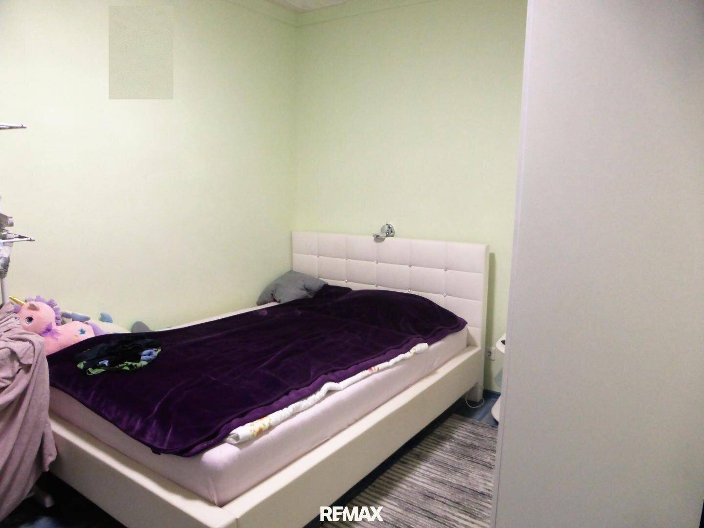 Helles Schlafzimmer mit weißem Bett, grünen Wänden und einfacher Einrichtung.