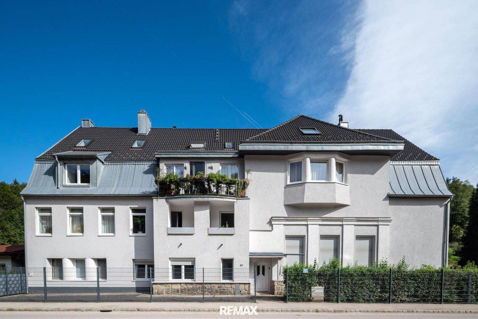 Mehrstöckiges Wohngebäude mit klassischer Fassade, kleinen Balkonen und Mansarddach unter blauem Himmel.