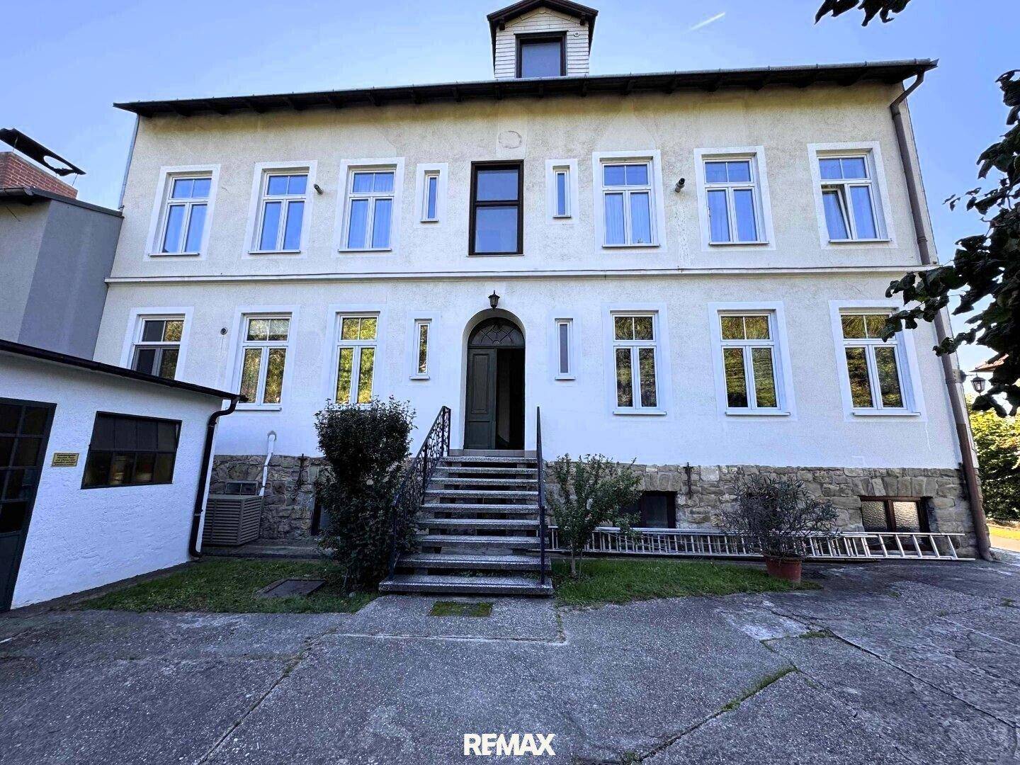 Vorderansicht des Gebäudes mit Haupteingang, Steintreppe und symmetrischen Fenstern.