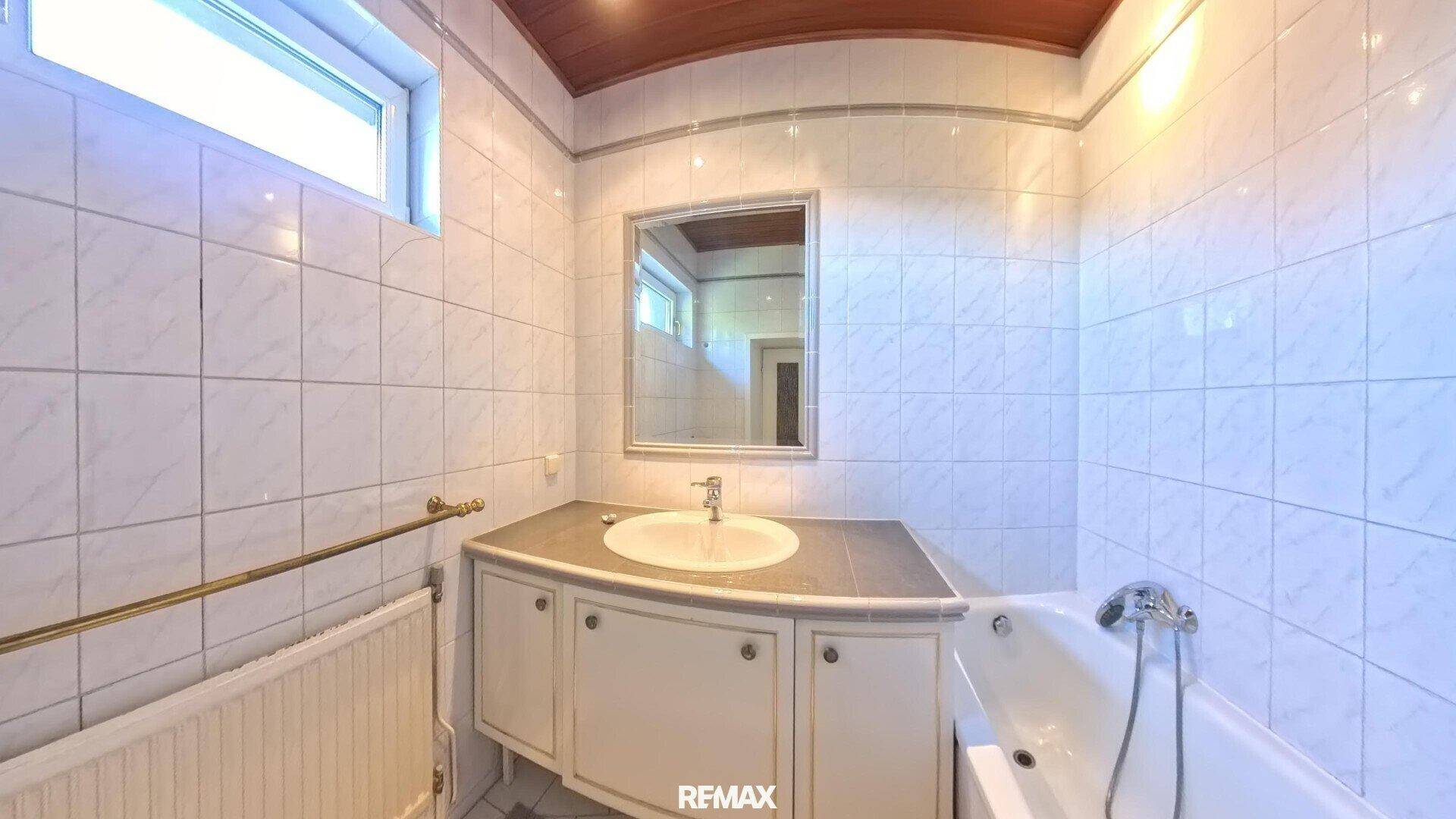 Gefliestes Badezimmer mit Badewanne, Einzelwaschbecken und einem kleinen Fenster für natürliche Belüftung.