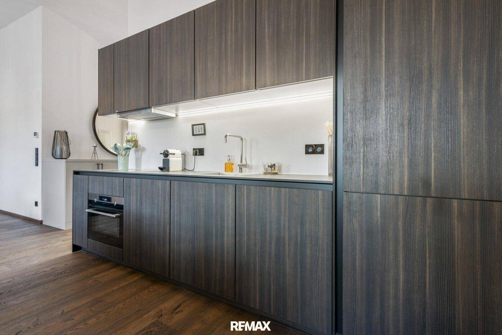Moderne Einbauküche mit dunklen Holzfronten, integrierten Geräten und indirekter Beleuchtung.