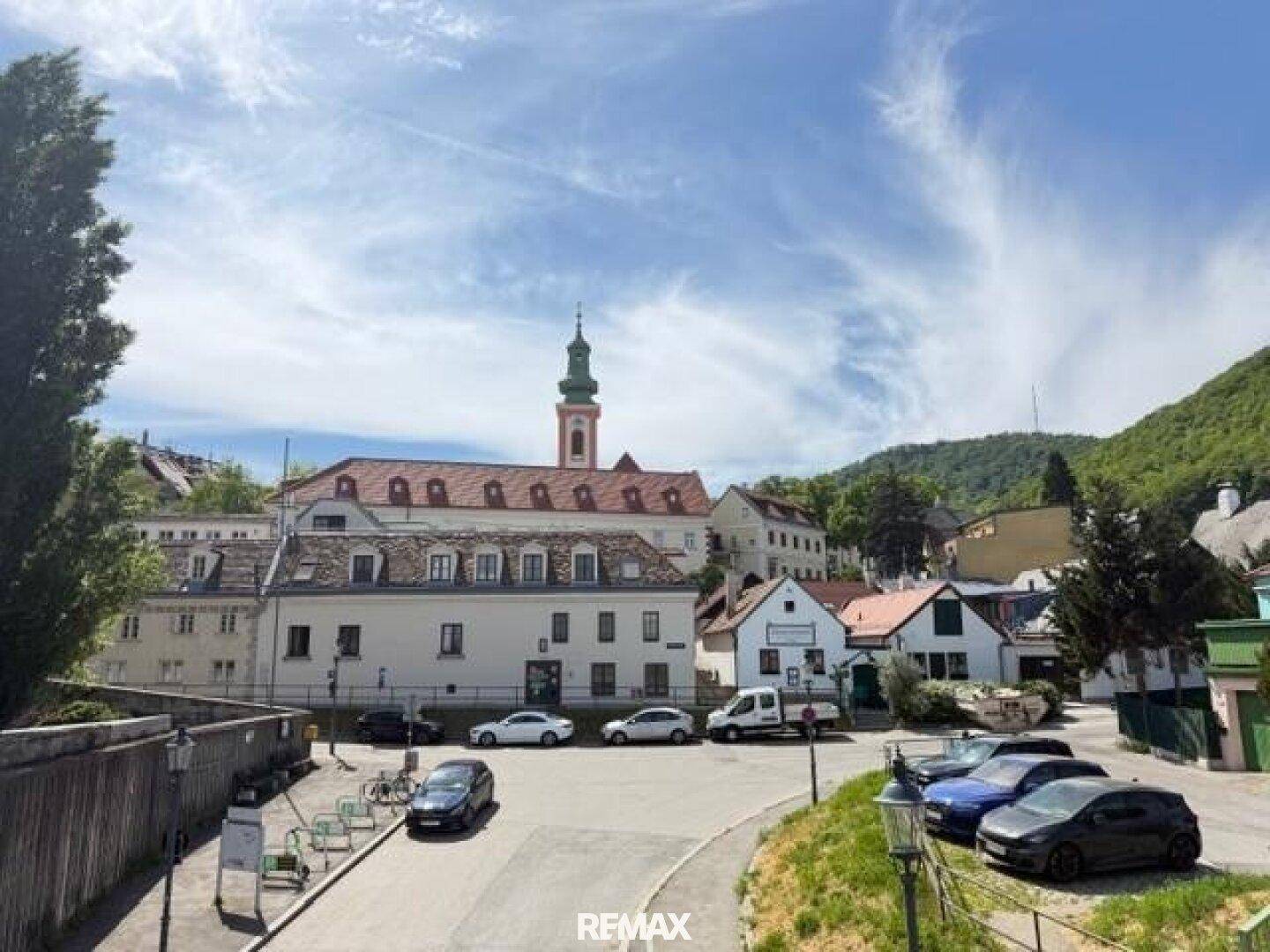 Historisches Dorf mit Kirche, traditionellen Gebäuden und grünen Hügeln im Hintergrund.