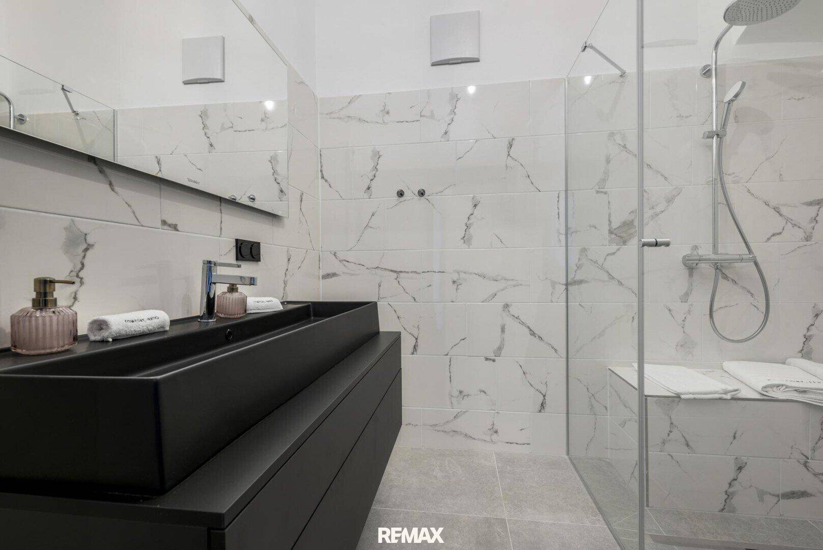 Modernes Badezimmer mit Marmorfliesen, schwarzem Waschtisch und begehbarer Dusche.