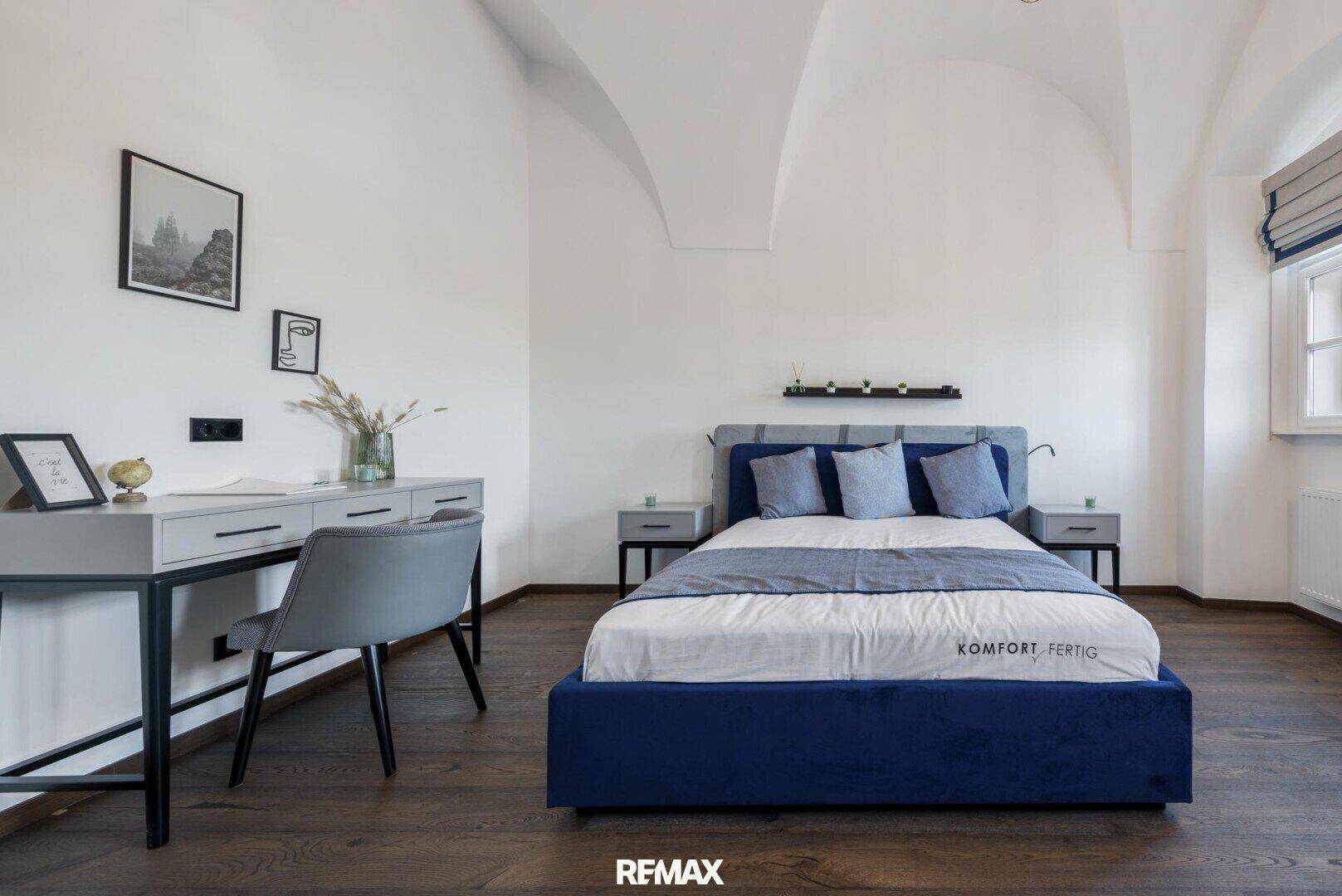 Modernes Schlafzimmer mit blauem Bett, Nachttischen und einem eleganten Schreibtisch.