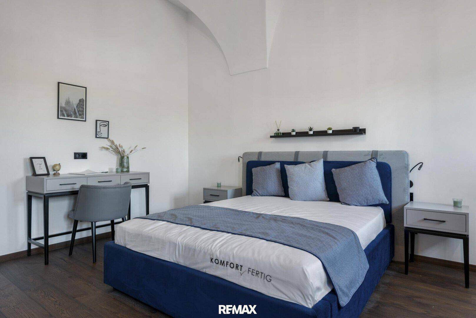 Helles Schlafzimmer mit Doppelbett, Schreibtisch und Holzboden unter einer gewölbten Decke.