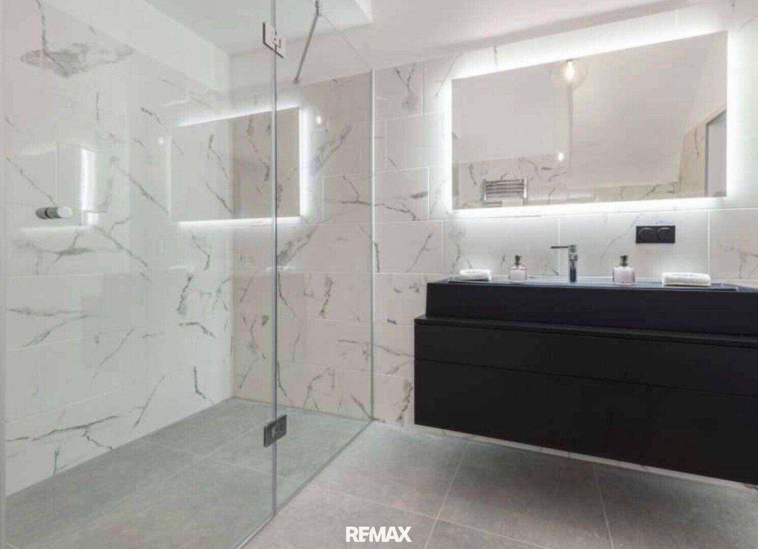 Elegantes Badezimmer mit beleuchtetem Spiegel, schwarzem Waschtisch und Glasdusche.