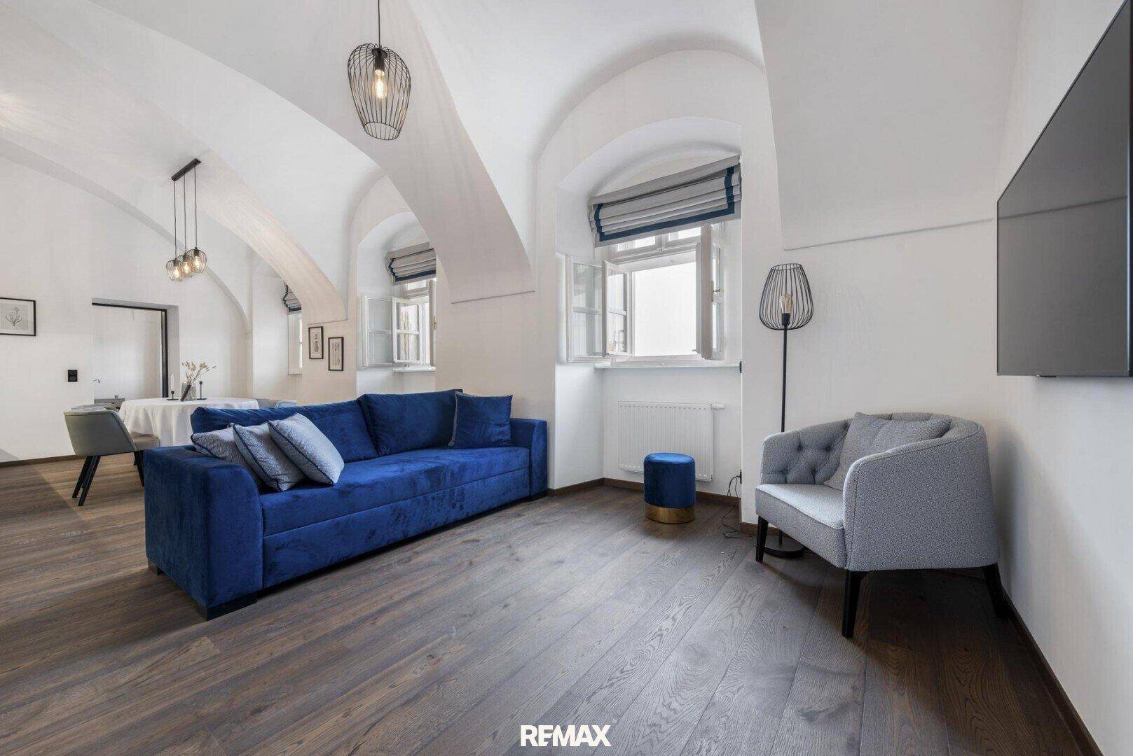Geräumiger Wohn-Essbereich mit blauer Couch, Holzboden und markanter gewölbter Decke.