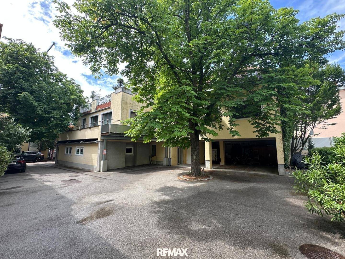 Außenansicht des Gebäudes mit Parkplätzen und viel Grün, umgeben von Bäumen.