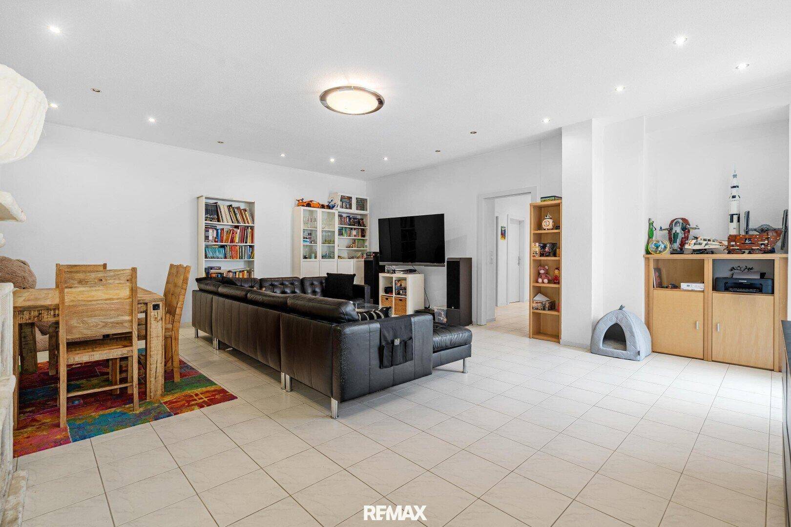 Geräumiges Wohnzimmer mit großem Sofa, Esstisch und Fliesenboden, hell und offen.