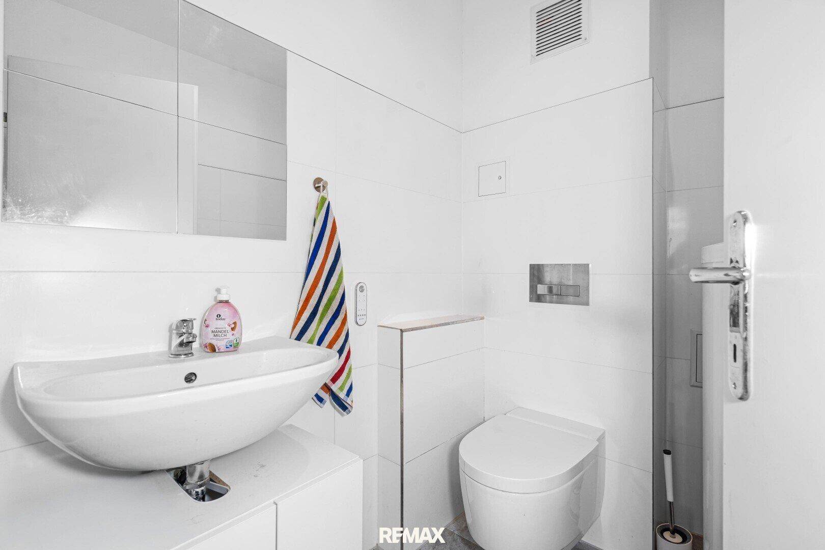 Modernes Gäste-WC mit weißem Waschbecken, Wand-WC und Fliesen an den Wänden.