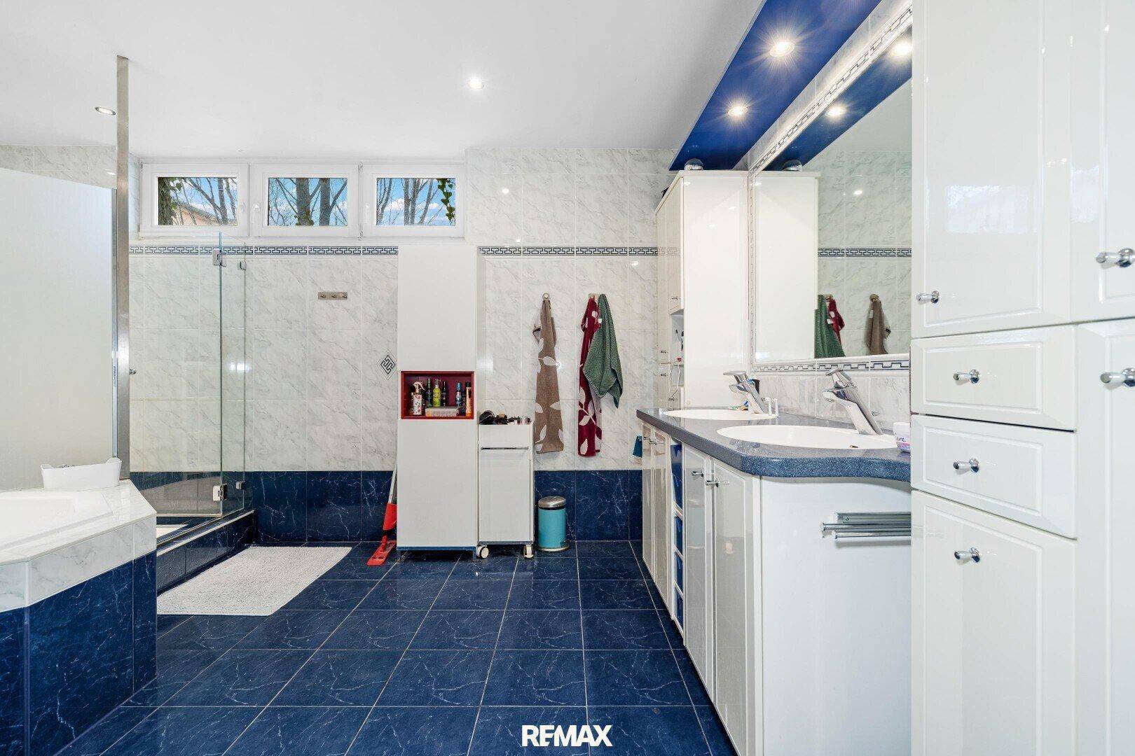 Helles Badezimmer mit Doppelwaschbecken, Badewanne, Dusche und Fenster.
