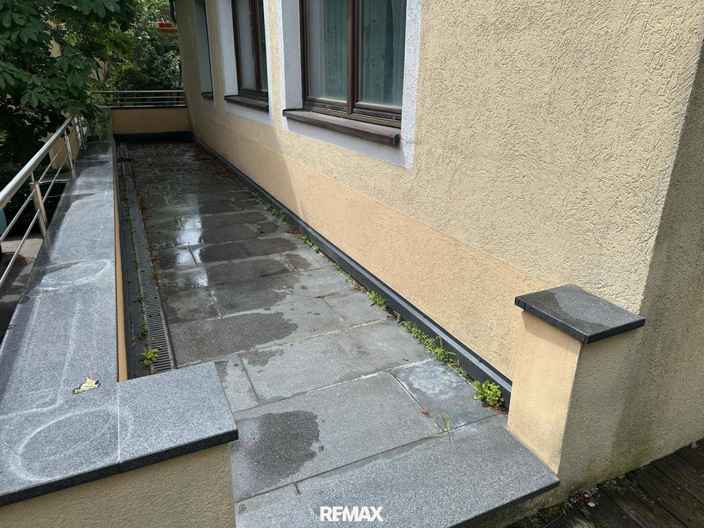 Gedeckte Terrasse mit Steinplatten und Geländer, direkt am Gebäude gelegen.