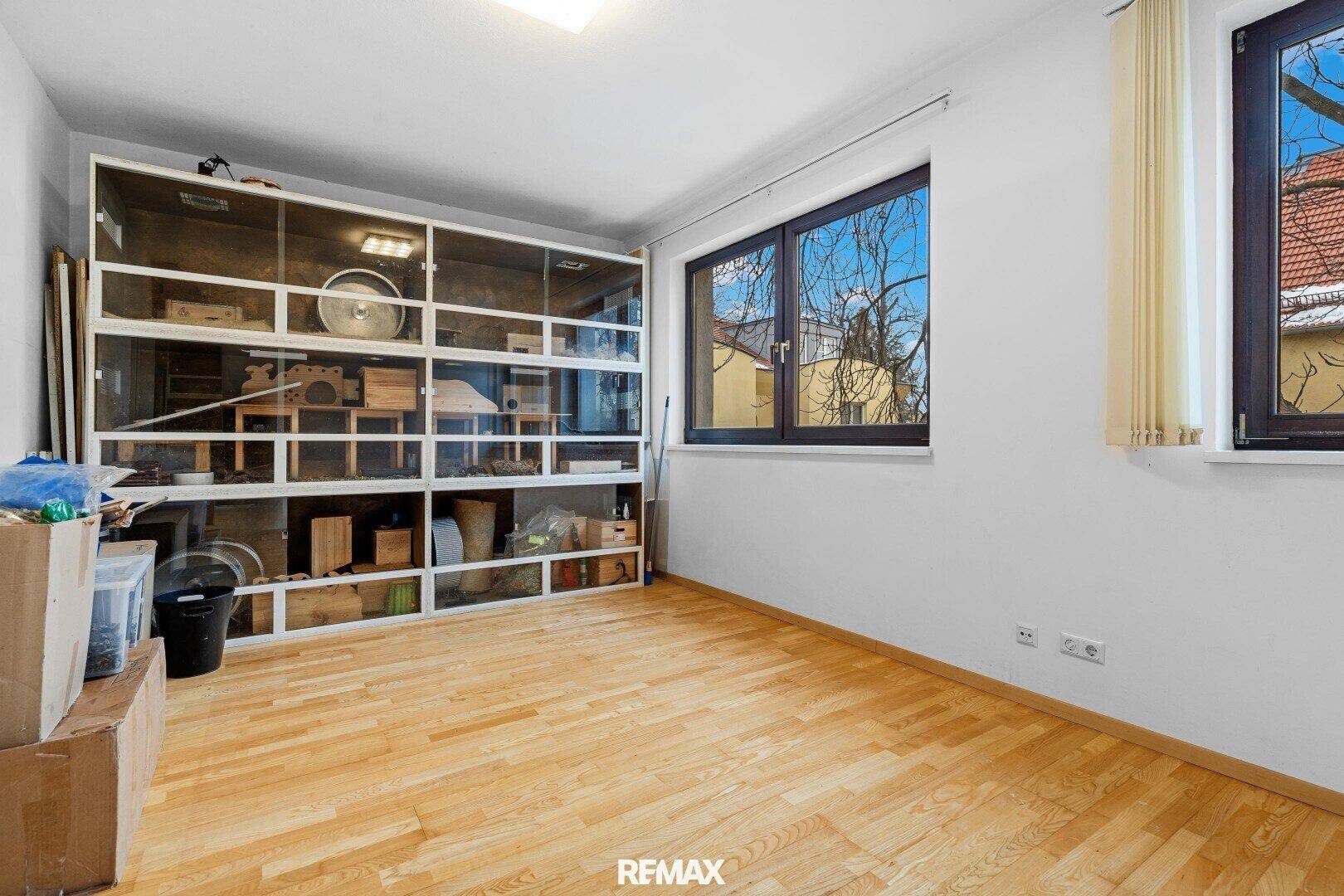 Helles Zimmer mit Holzboden und großem Terrarium oder Vitrine, mit Blick nach draußen.