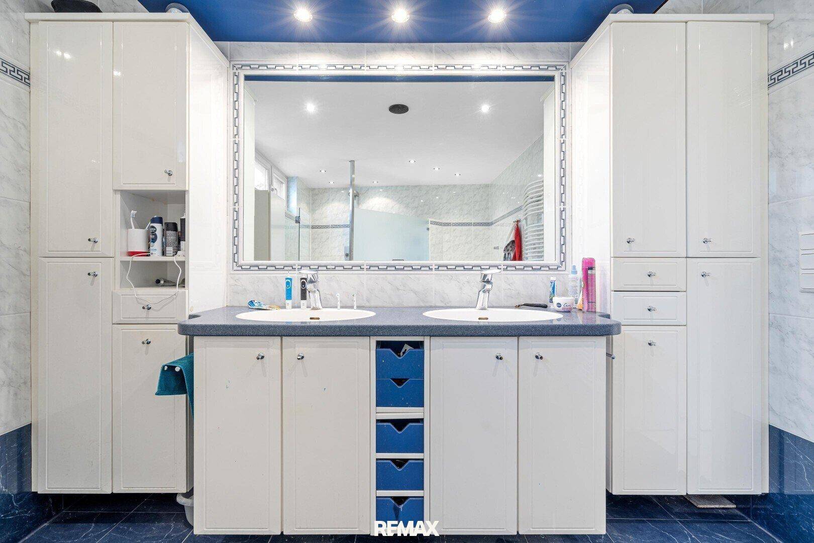 Badezimmer mit Doppelwaschbecken, großem Spiegel und blauen Akzenten.