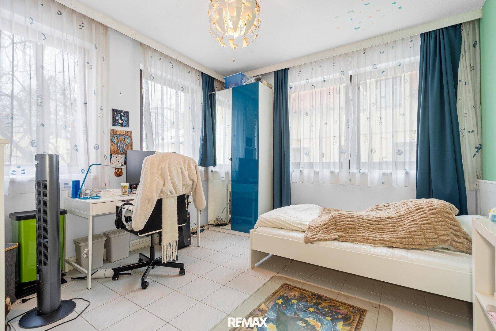 Kinderzimmer mit Schreibtisch, Bett und farbenfroher Dekoration, gut beleuchtet.