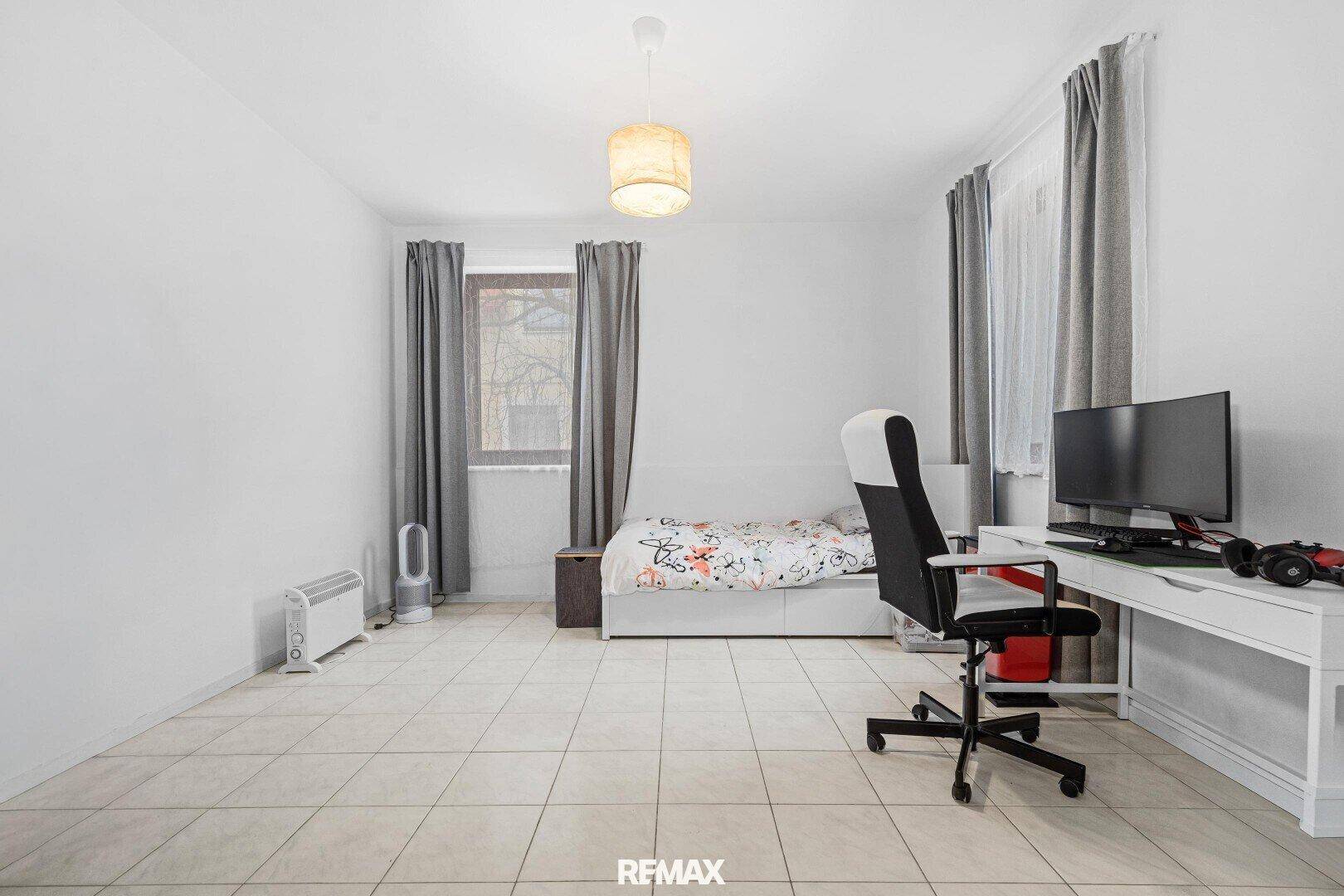Schlafzimmer mit Einzelbett, Schreibtisch und Fliesenboden, hell und funktional eingerichtet.