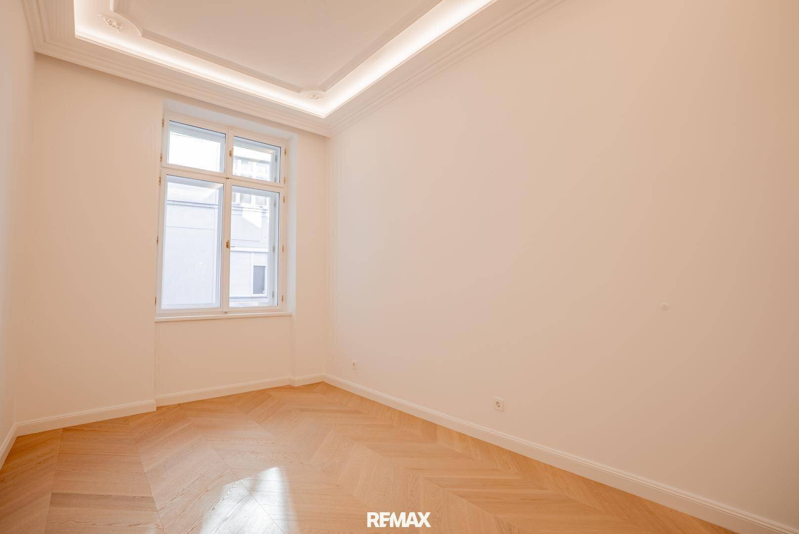 Heller Raum mit Fischgrätparkett, Stuckdecke und großem Fenster für viel Licht.