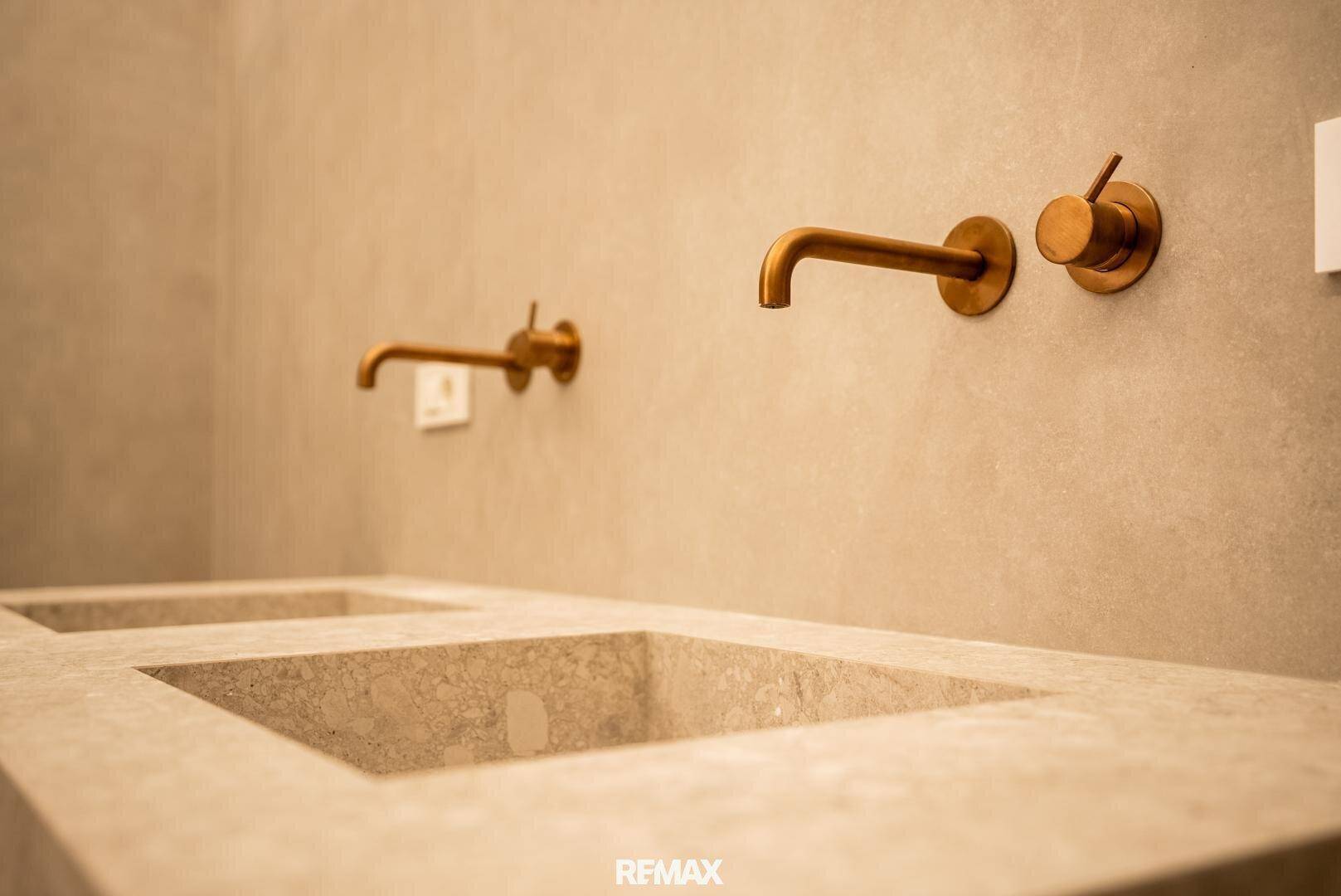 Modernes Badezimmer mit zwei integrierten Waschbecken und eleganten Wandarmaturen in Bronze.