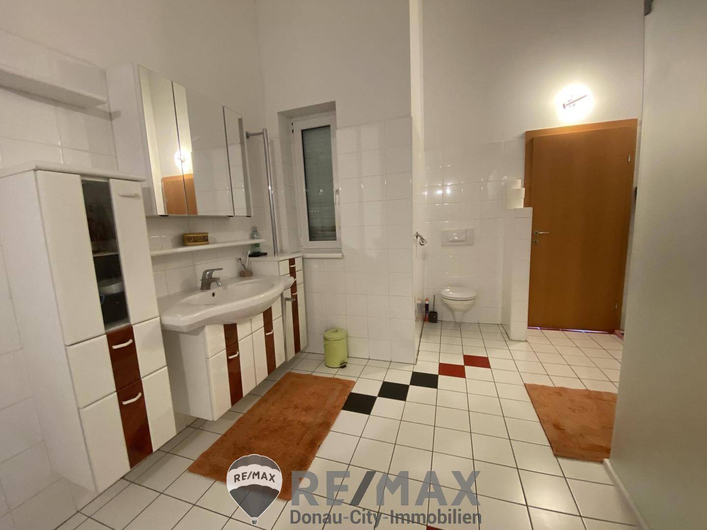 Geräumiges Badezimmer mit weißen Fliesen, Waschbecken und separatem Duschbereich.