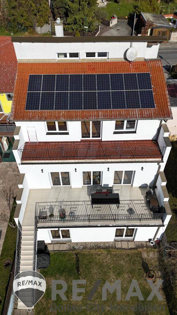 Luftaufnahme eines modernen Hauses mit Photovoltaikanlage auf dem Ziegeldach und Terrassen, effizient und geräumig.