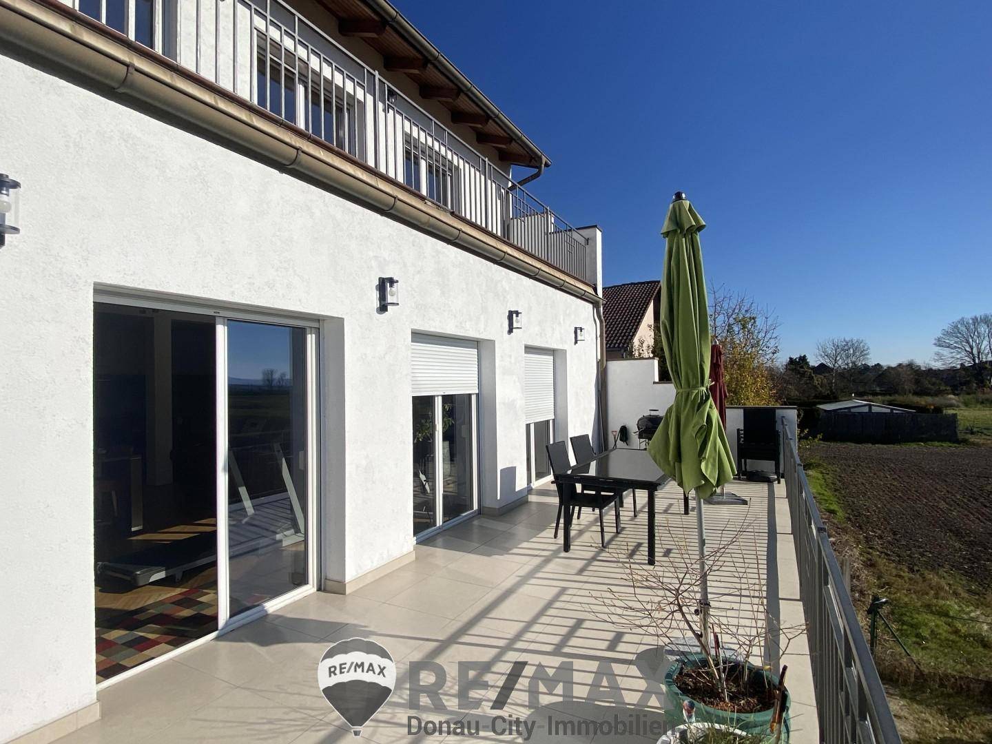 Große Terrasse mit Fliesenboden, Gartenmöbeln und weitem Blick über die Felder.
