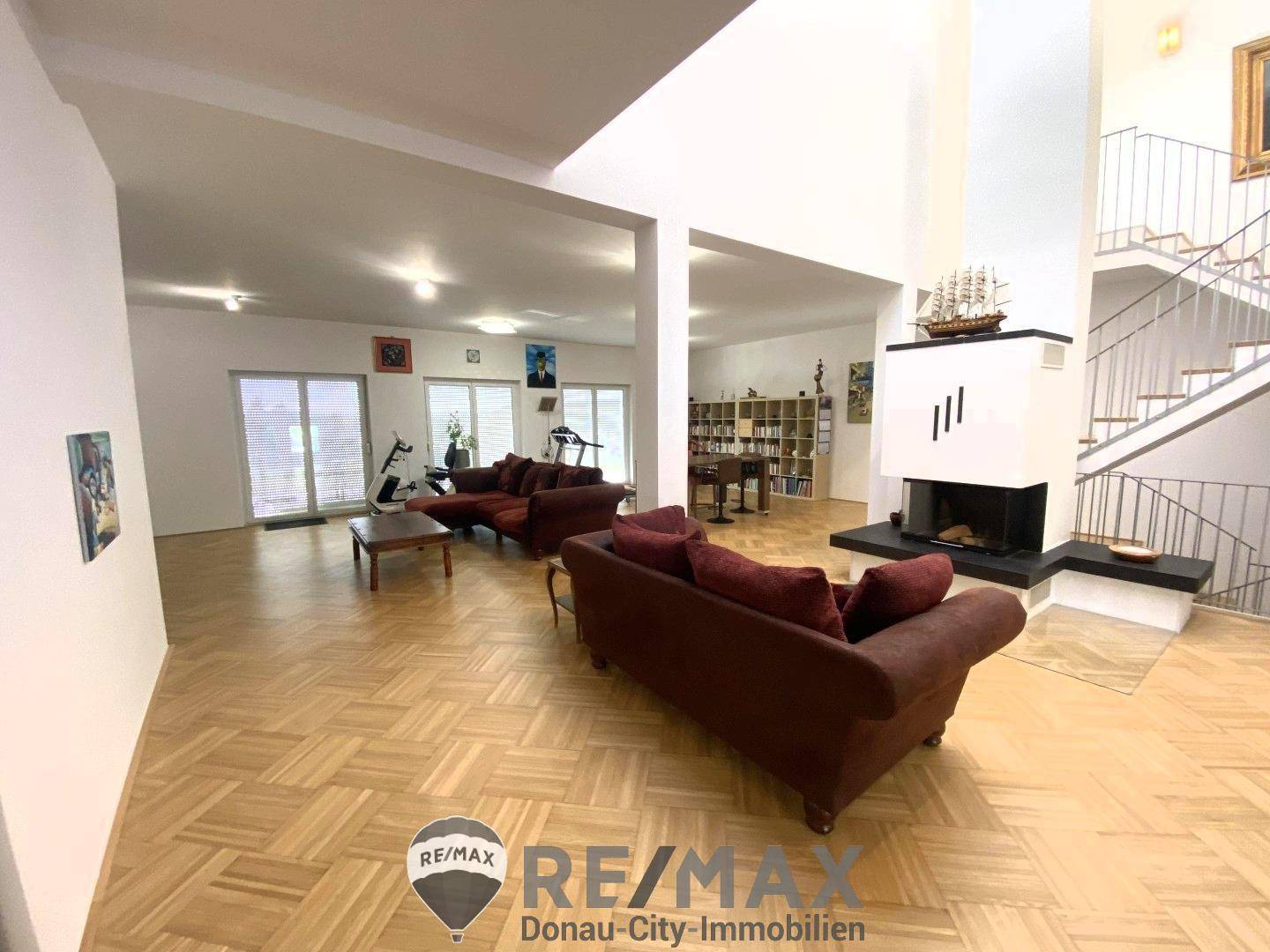 Großzügiges Wohnzimmer mit Parkettboden, Kamin und offener Treppe zum Obergeschoss.