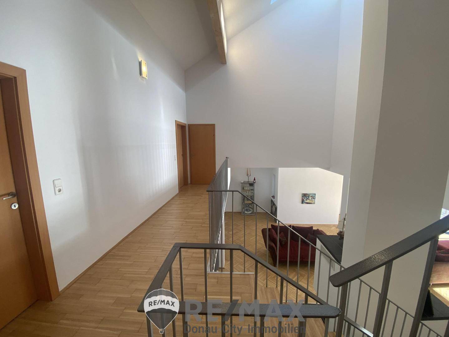Heller Flur im Obergeschoss mit Holzparkett und Blick auf den darunterliegenden Wohnbereich.