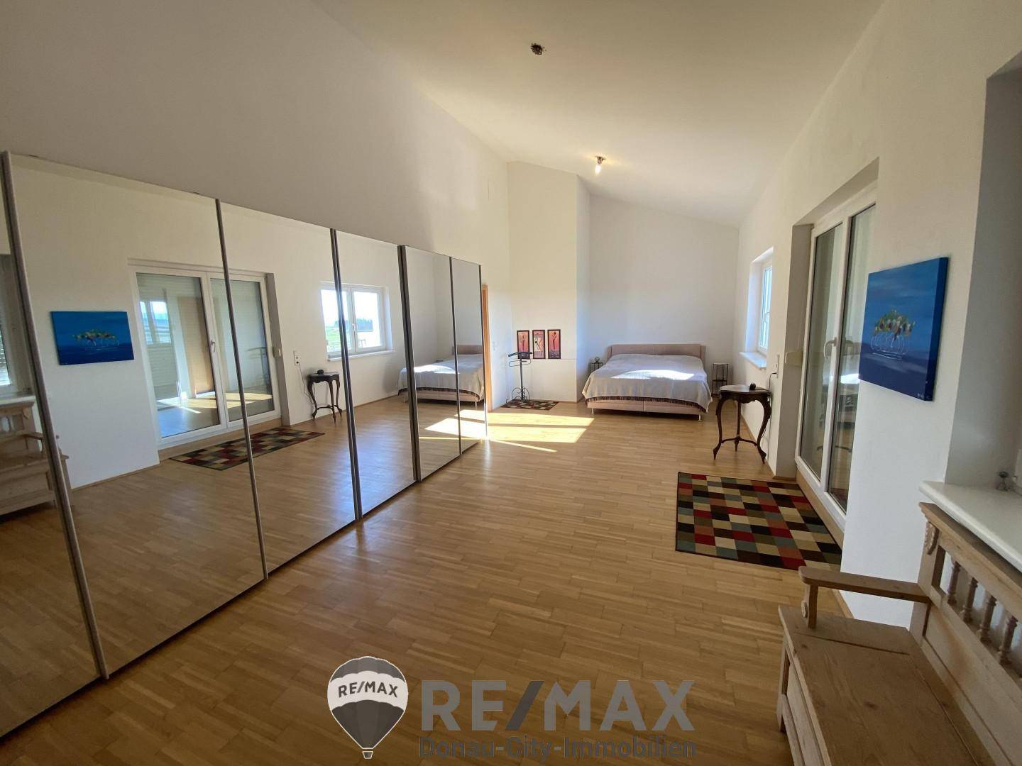 Großes Schlafzimmer mit Parkettboden, Spiegelschränken und Zugang zu einem Balkon.