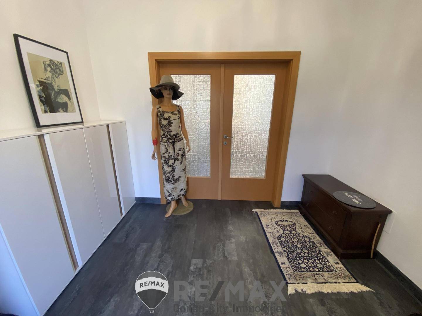 Heller Flur mit dunklem Fliesenboden, Garderobenschrank und dekorativer Schaufensterpuppe.