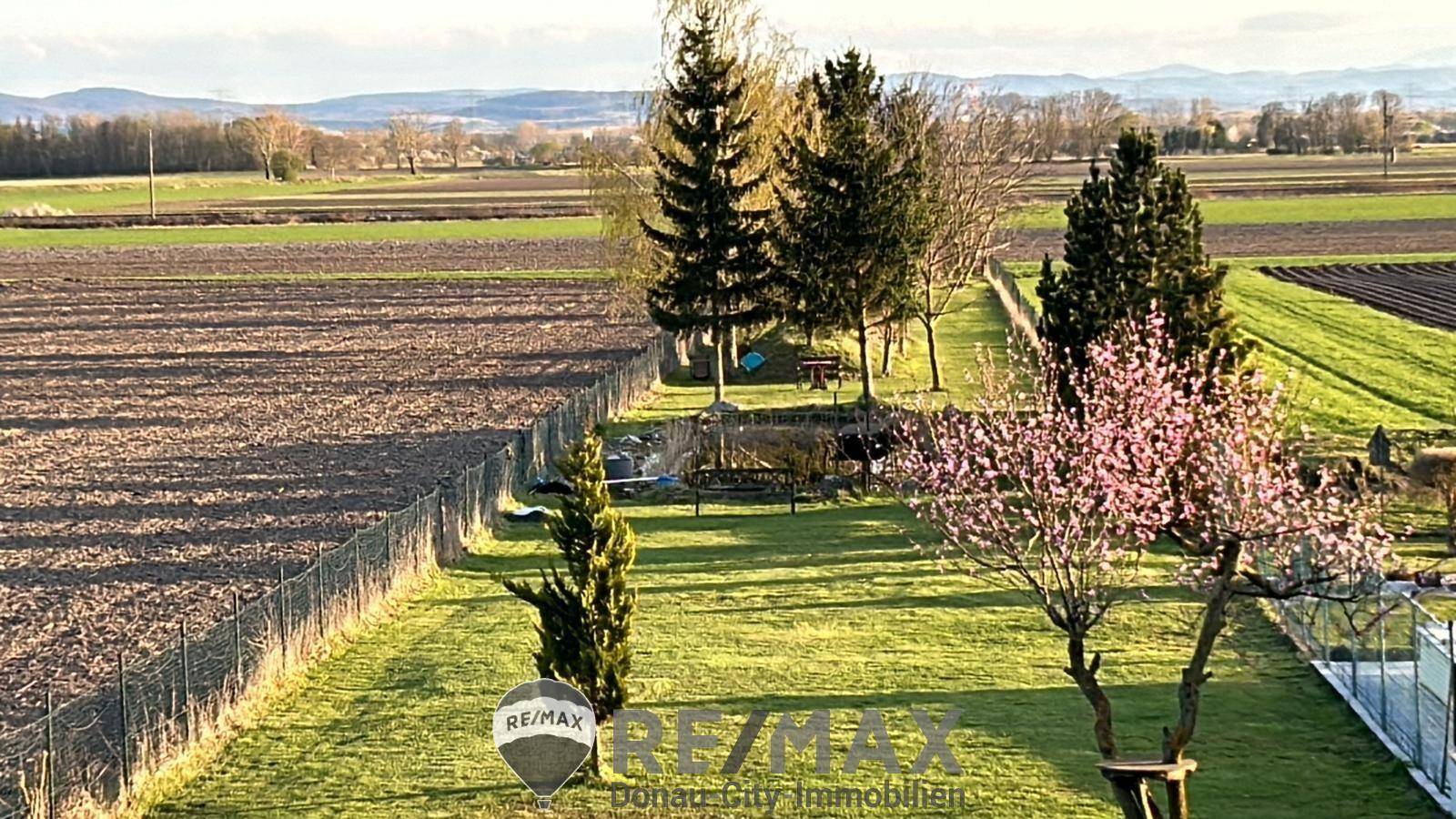 Weitläufiger Garten mit Rasenfläche, blühenden Bäumen und Blick auf die umliegende Landschaft.