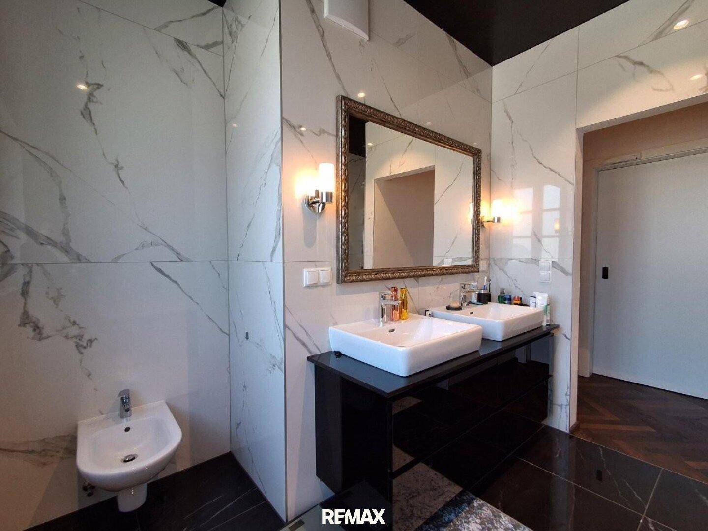 Luxuriöses Badezimmer mit Marmorfliesen, Doppelwaschbecken, Bidet und großem Spiegel.